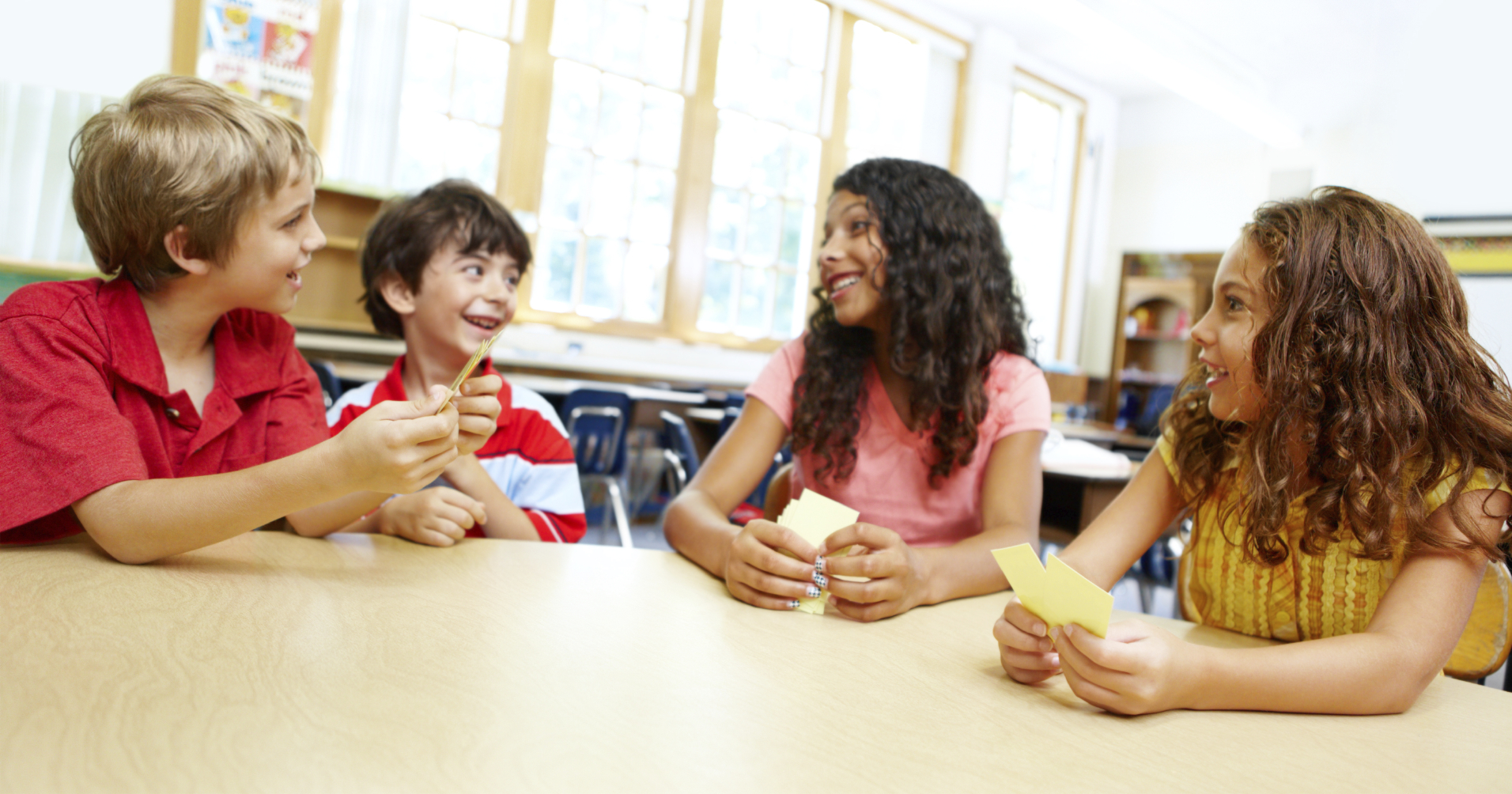 Image of Four young children playing cards in their classroom together