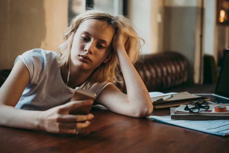 Female student turning away from her schoolwork to look at her phone.