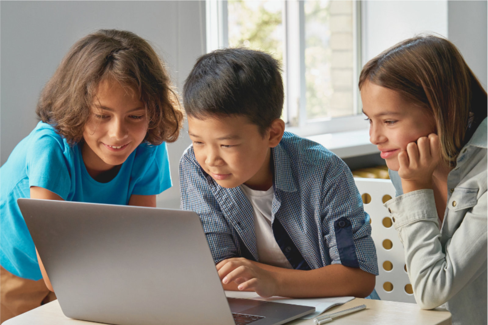 Students collaborating around a laptop in a classroom, exploring content together and sharing ideas.