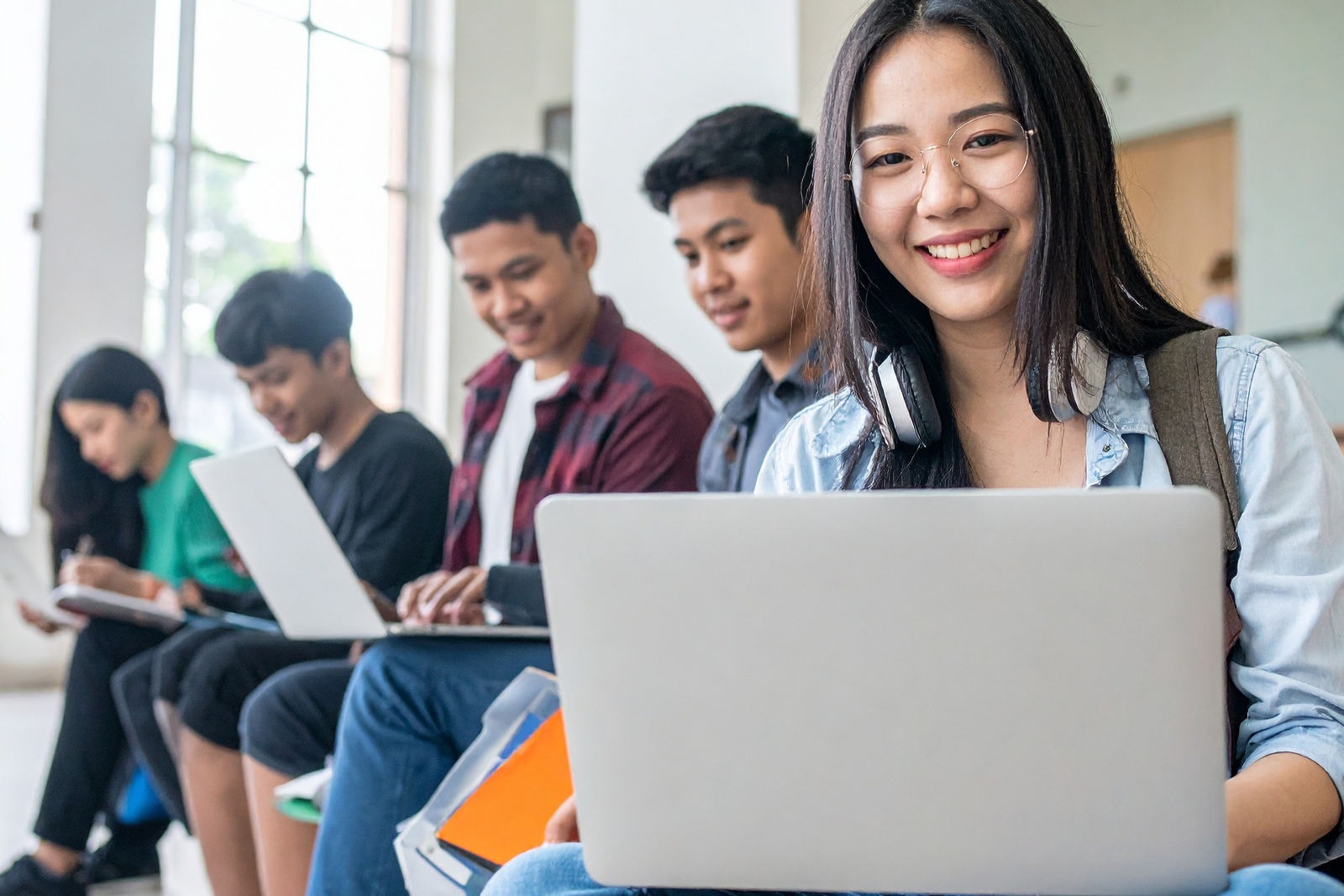 Student using a laptop in a post-secondary setting, with peers studying in the background