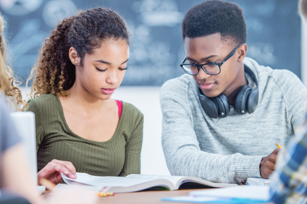 High school students reading and discussing a textbook together in a classroom.”